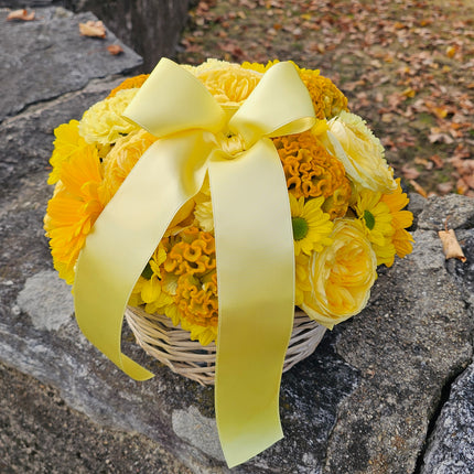 Sonniges Blumenarrangement in Gelb, Creme und Orange im geflochtenen Korb
