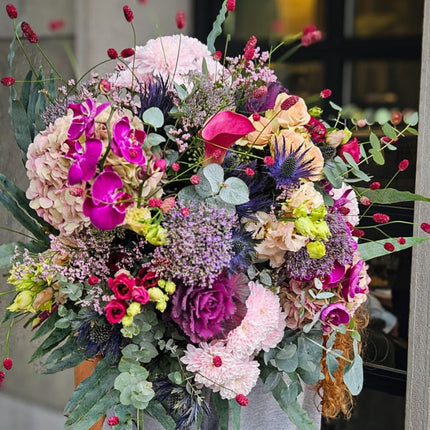 Modern gebundener Blumenstrauss mit pinken Orchideen, zarten Hortensien, violetten Disteln und dekorativen roten Blütenständen als besonderes Blumengeschenk aus Zürich.