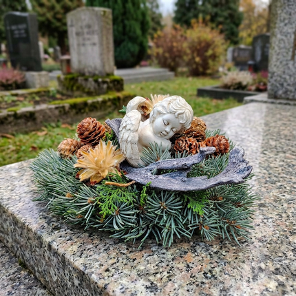 Natürliches Trauerherz für Allerheiligen mit hellem Engel, Tannengrün, braunen Zapfen und rustikalen Holzelementen als Grabschmuck bei Blumen Krämer Zürich.